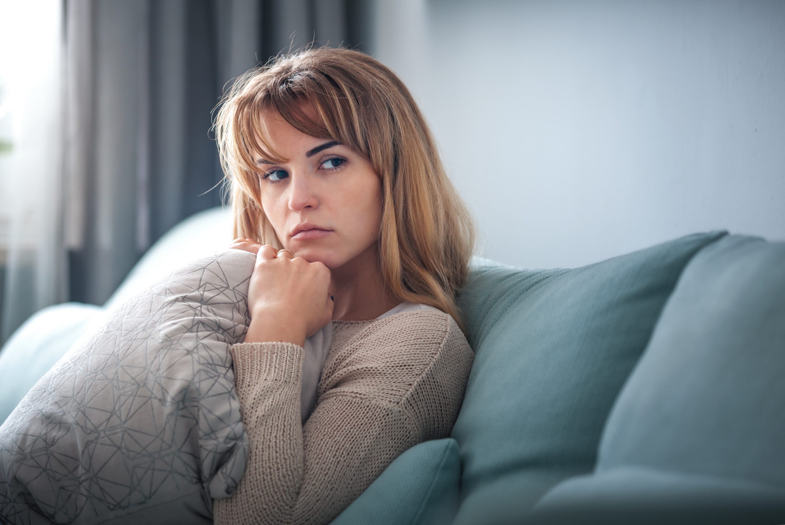 Depressed woman sitting on sofa at home, thinking about important things